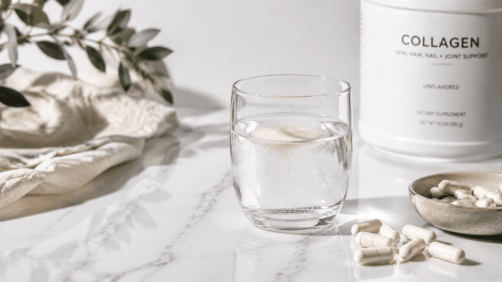 Bicchiere di vetro con integratore di collagene disciolto in acqua accanto a capsule di collagene